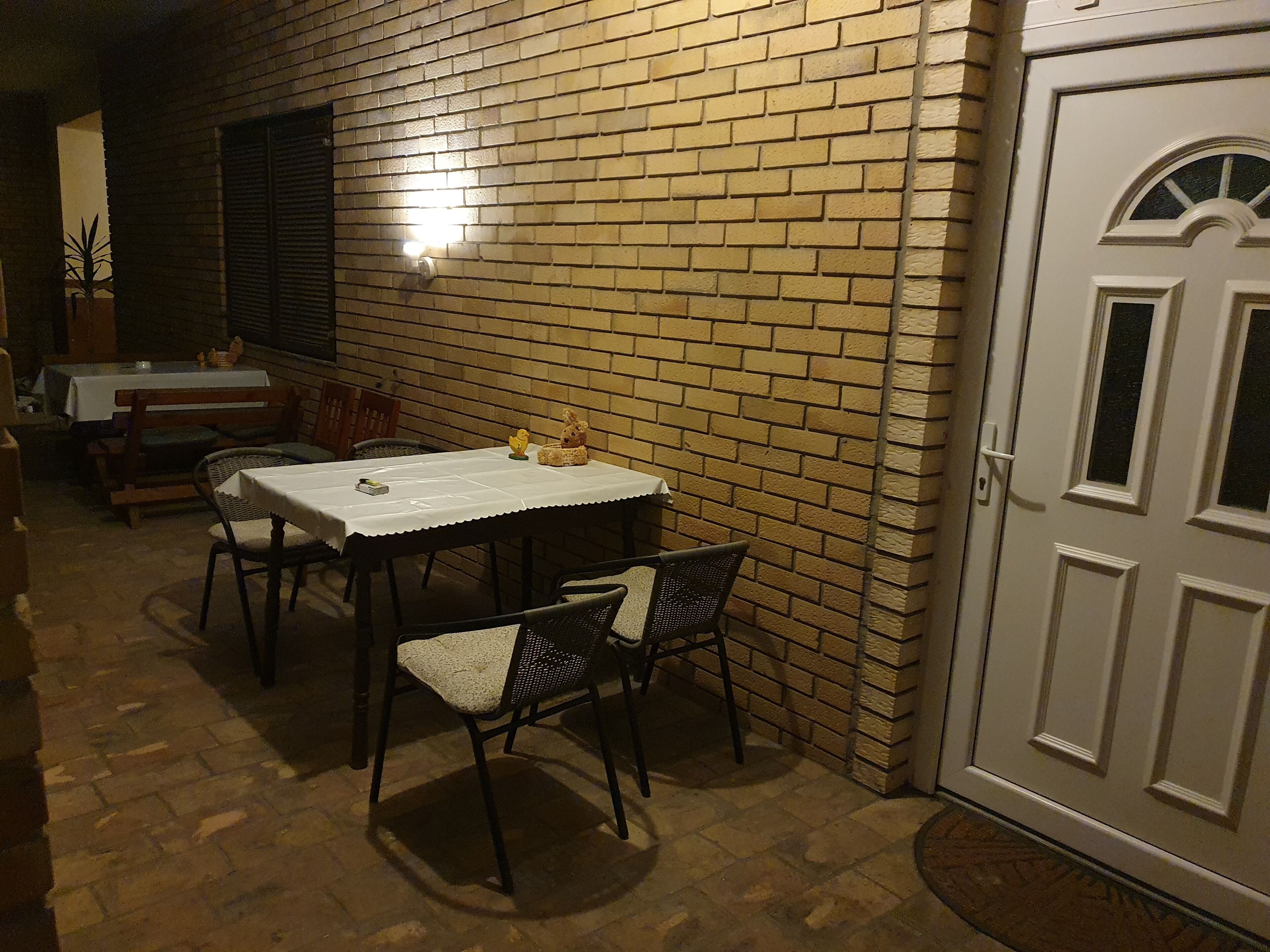 Patio esterno con tavolo e sedie, un muro in mattoni e una porta.