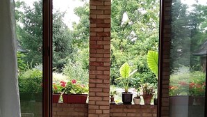 A room with a large window overlooking a garden with potted plants and a brick wall. - Citadela - Large Double Room (Sombor)