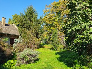 A stone house with a chimney, surrounded by a lush garden with various trees and shrubs. - Citadela - Large Double Room (Sombor)