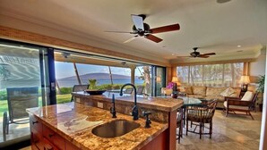 A kitchen with a granite countertop, a sink, and a dining area with a table and chairs. - Luxury Oceanfront Escape – King Suite, Large Lanai & 30 Seconds to Beach (Lahaina)