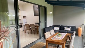 A modern living room with a sofa, a wooden table, and a dining area with chairs. - Baden 86 - Rainbow Shores. Walk To Beach - Top Floor - Air conditioned Unit. Free Wi-Fi (RAINBOW BEACH)