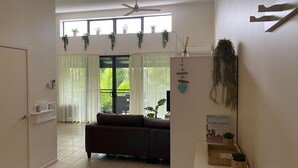 A living room with a sofa, a ceiling fan, and a view of the outdoors through large windows. - Baden 86 - Rainbow Shores. Walk To Beach - Top Floor - Air conditioned Unit. Free Wi-Fi (RAINBOW BEACH)