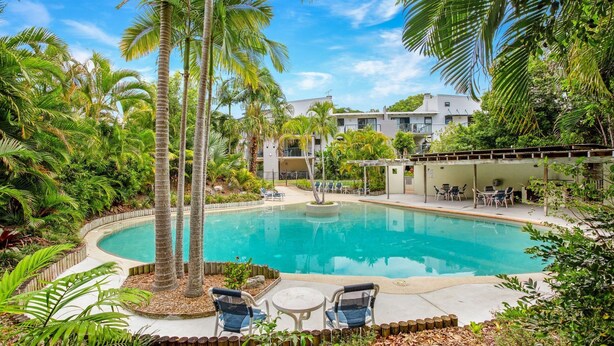 A pool surrounded by palm trees and greenery, with lounge chairs and a building in the background. - Baden 86 - Rainbow Shores. Walk To Beach - Top Floor - Air conditioned Unit. Free Wi-Fi (RAINBOW BEACH)