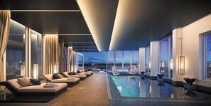 Et moderne poolområde indendørs med loungeområde og store vinduer der giver udsigt over byen.
