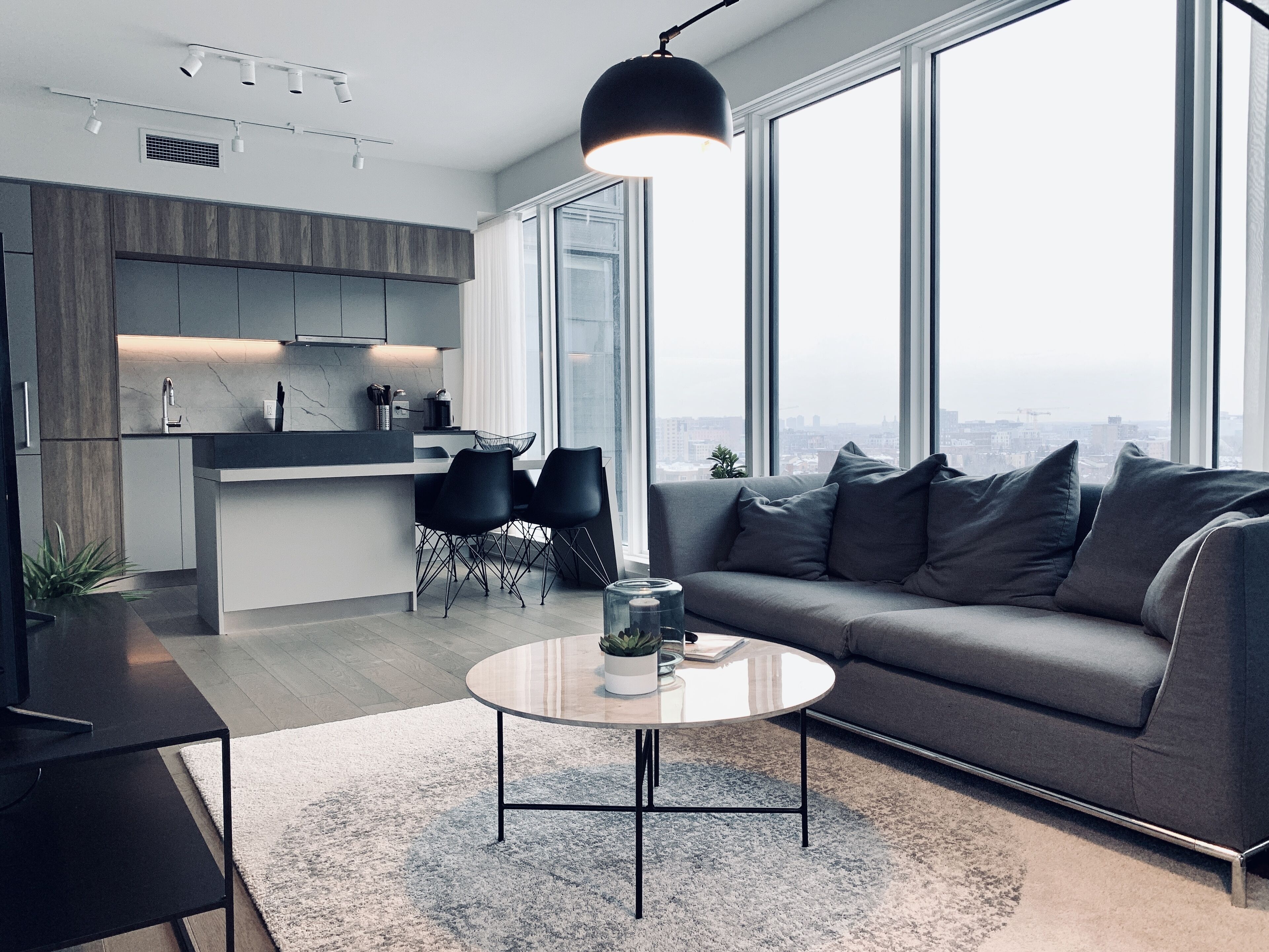 A modern living room with a grey sofa, a round coffee table, and a kitchen area with a dining set.
