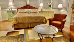 Un dormitorio con una cama grande, dos mesitas de noche con lámparas, un aparador, un sillón rojo y una mesa de centro de vidrio.