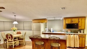 Una cocina moderna con armarios de madera, un refrigerador, un microondas y una zona de comedor con una mesa y sillas.