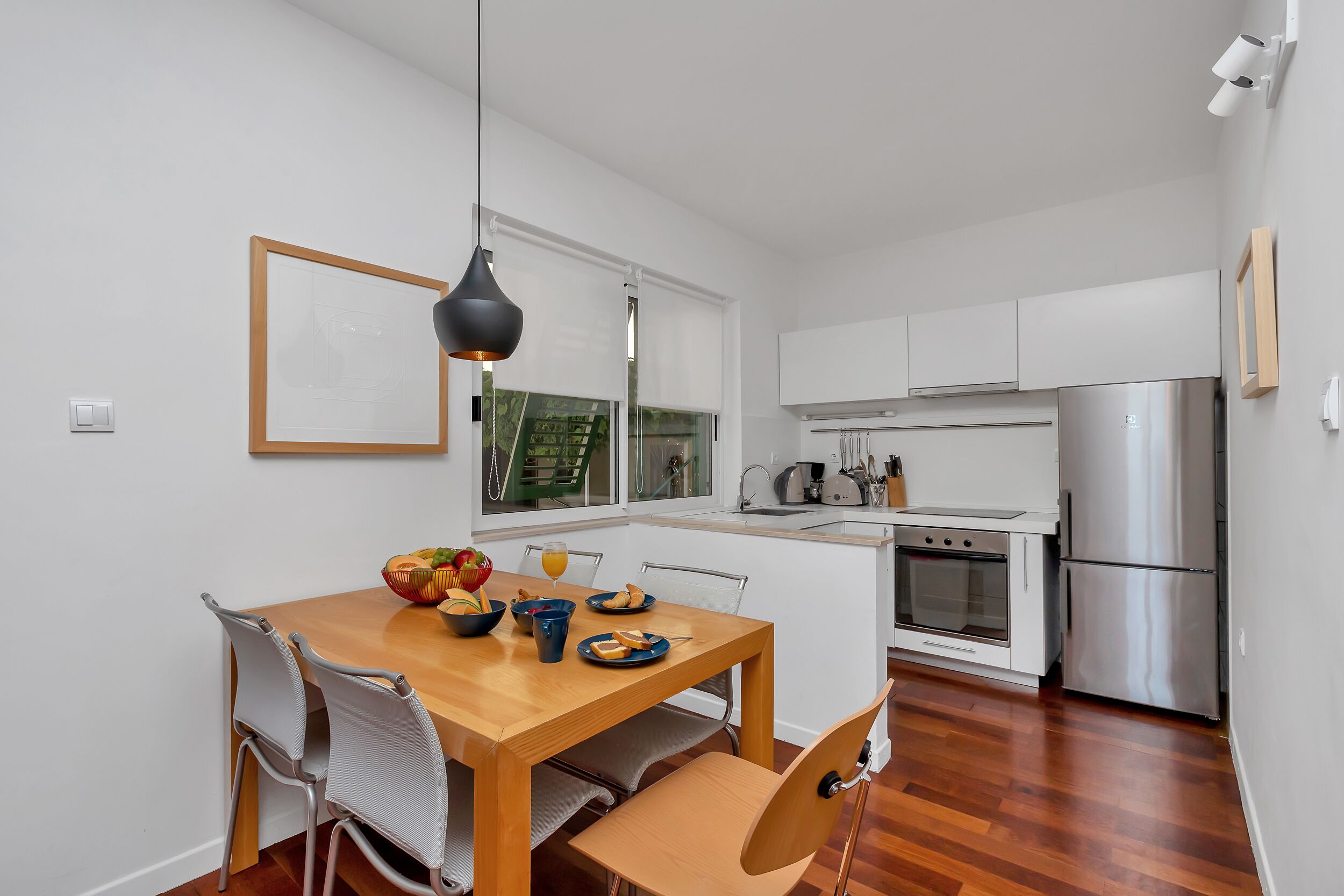 Een moderne keuken met witte kasten, roestvrijstalen apparatuur en een houten eettafel met stoelen.