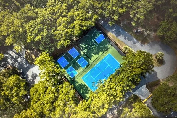 An aerial view of a tennis court surrounded by dense greenery.