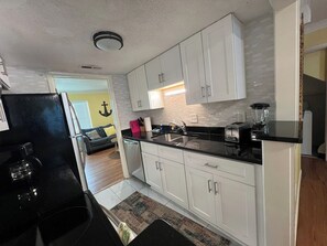 A compact kitchen with white cabinets, a black countertop, and a visible blender.
