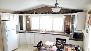 A kitchen with white cabinets, a dining table with chairs, a clock, and a window with curtains. - Randy's Rathbun Rental.  "Your Home Away From Home"  Fully Furnished Sleeps 6 (Moravia)