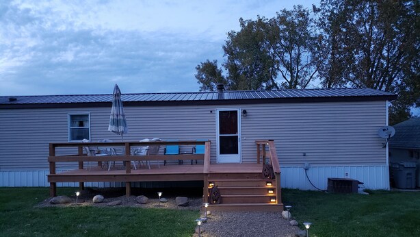 A wooden deck with outdoor seating, a gravel pathway with lights, and a house with a metal roof and siding. - Randy's Rathbun Rental.  "Your Home Away From Home"  Fully Furnished Sleeps 6 (Moravia)