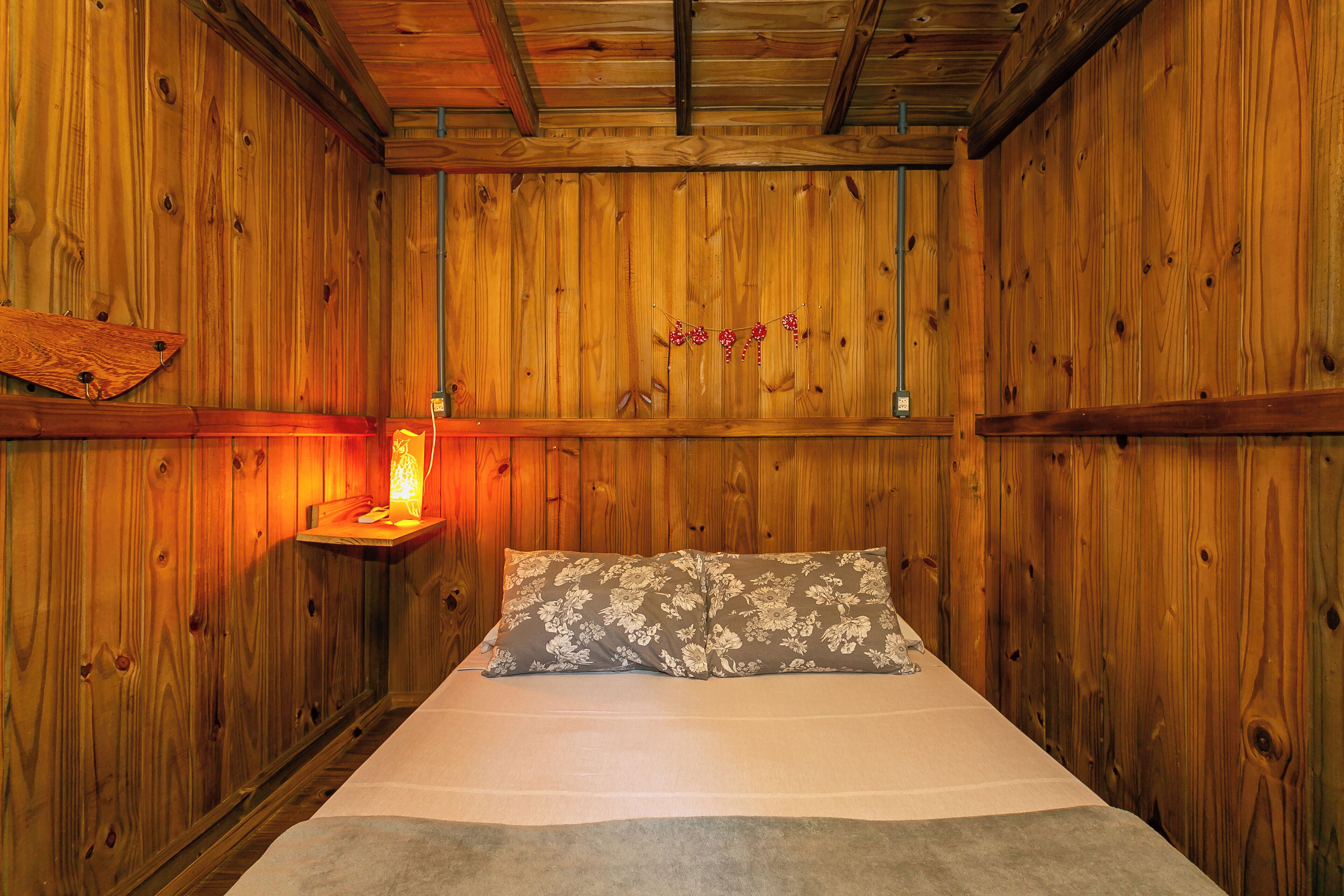 Habitación de madera con una cama, una mesita de noche con lámpara y una pared de madera con un letrero de 'Welcome'.