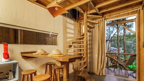 A rustic wooden interior with a wooden staircase, a dining table with stools, and a view of the outdoors through large windows. - Moradas do Vale Praia do Rosa (Imbituba)