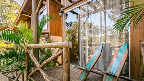 A wooden deck with a rustic wooden chair and a surfboard leaning against the wall. - Moradas do Vale Praia do Rosa (Imbituba)