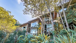 A wooden house with a deck surrounded by tropical plants. - Moradas do Vale Praia do Rosa (Imbituba)
