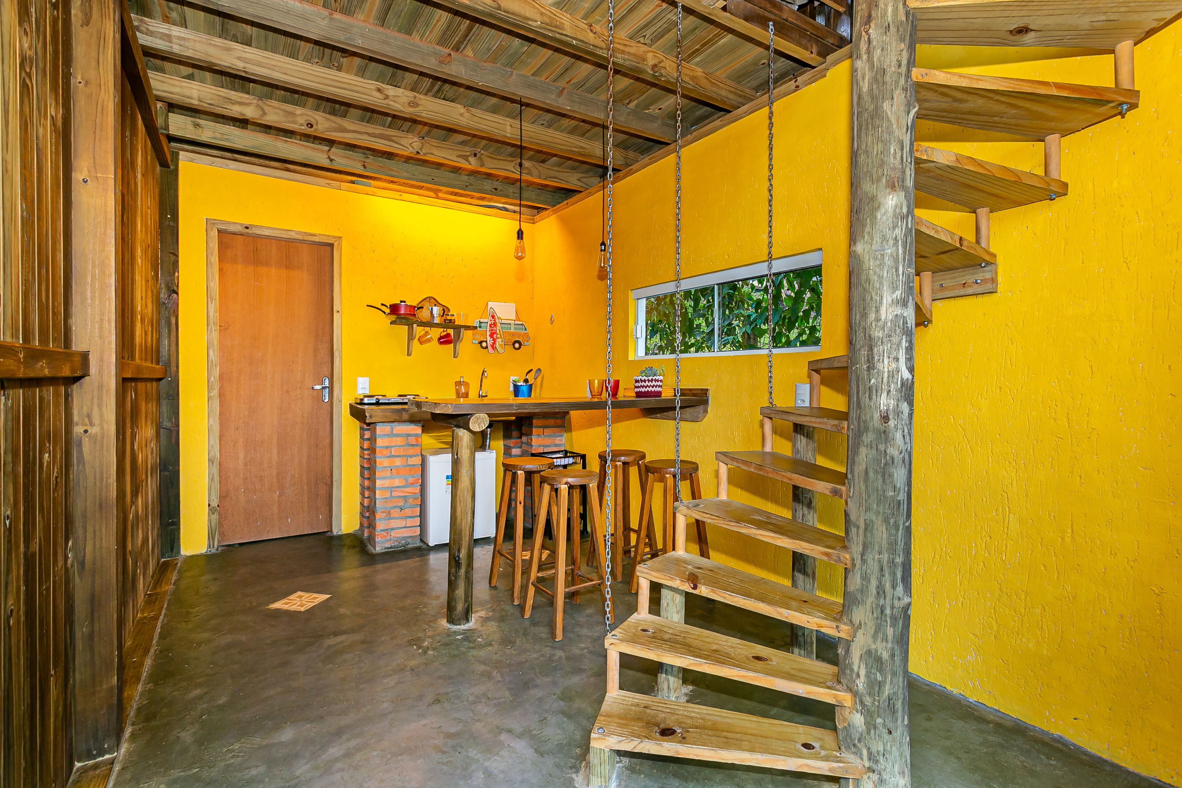 Une pièce avec un mur jaune, un escalier en bois et un coin bar avec des tabourets.