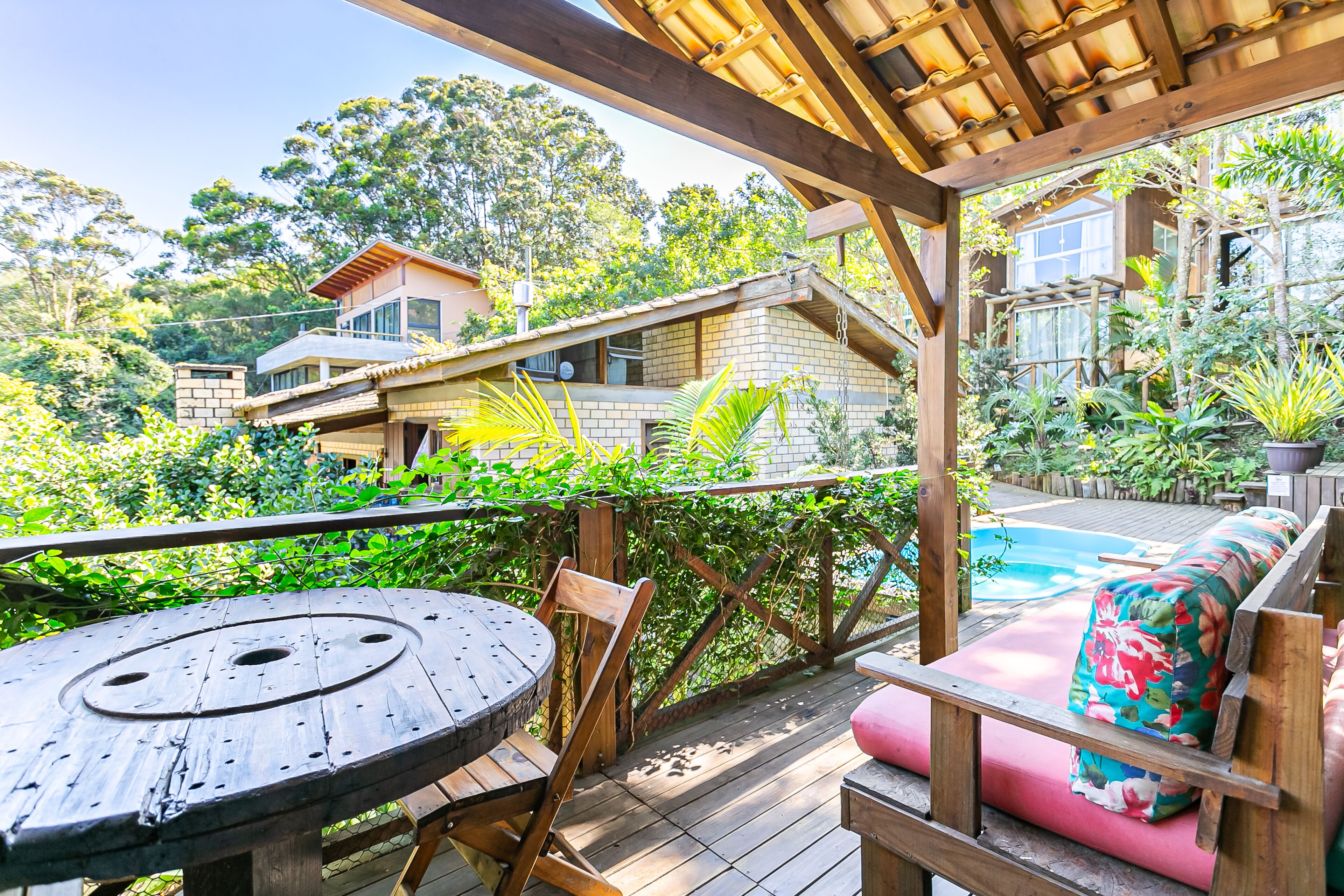 Une terrasse en bois avec une table ronde et des chaises, un banc rembourré, et une piscine en arrière-plan.