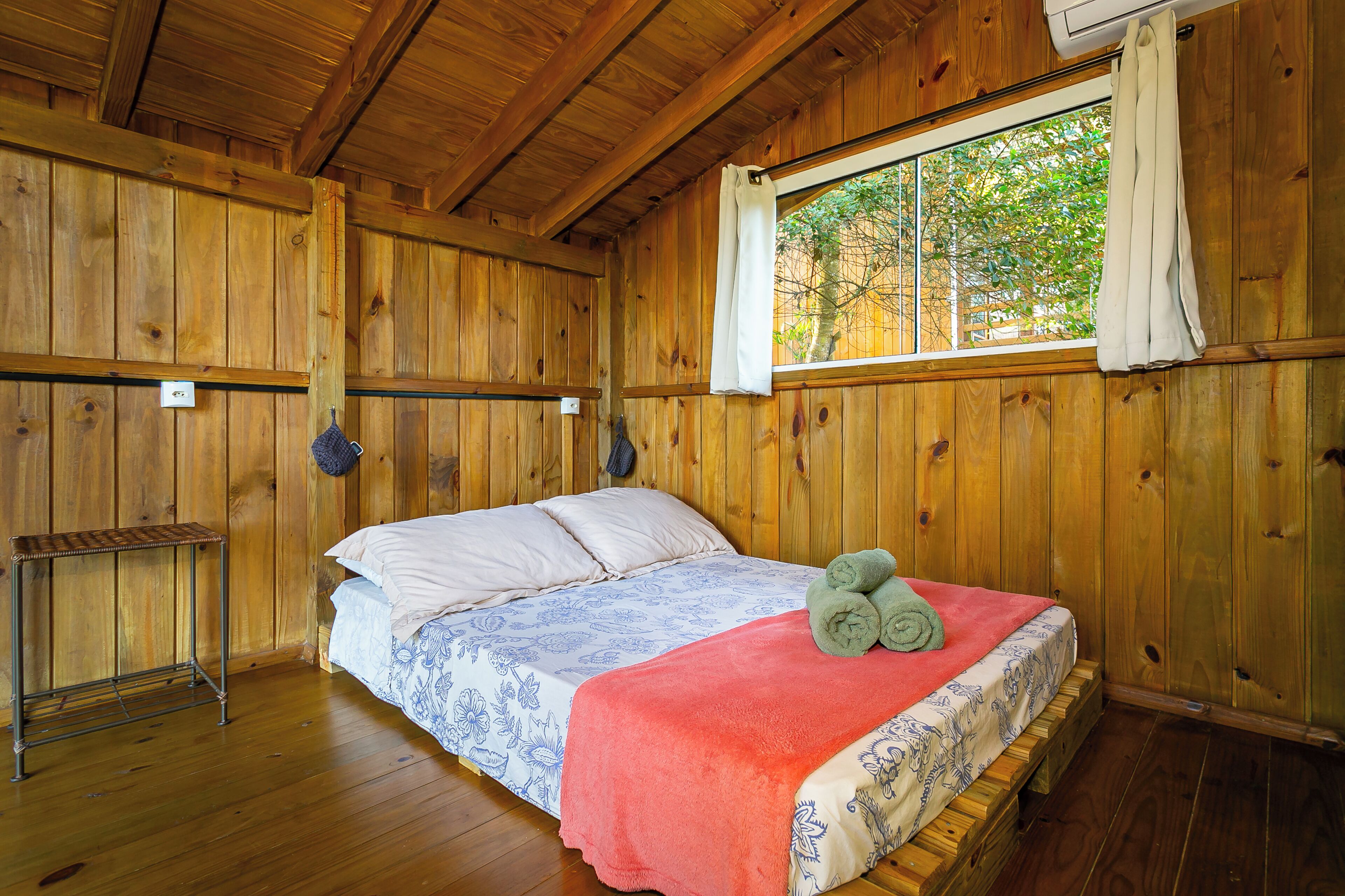 A wooden cabin room with a bed, a window, and a small table.
