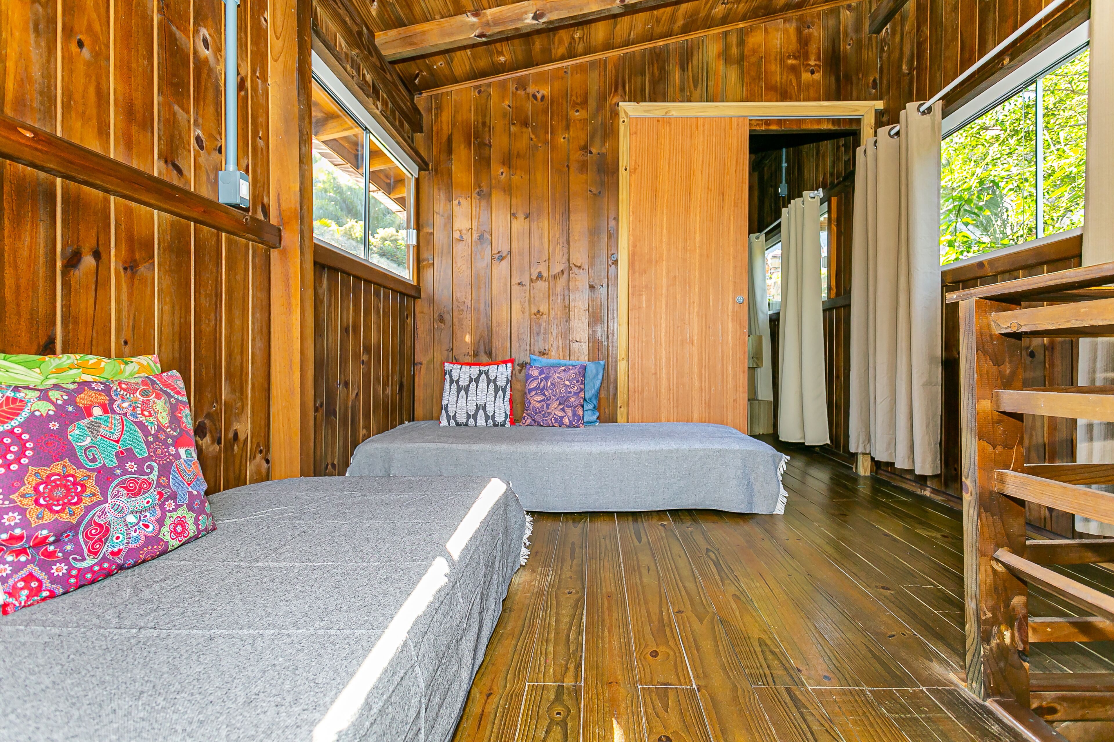 Una cabaña de madera con dos camas, un banco y una ventana con cortinas.