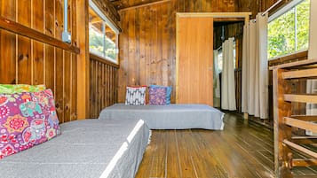 Una cabaña de madera con dos camas, un banco y una ventana con cortinas.