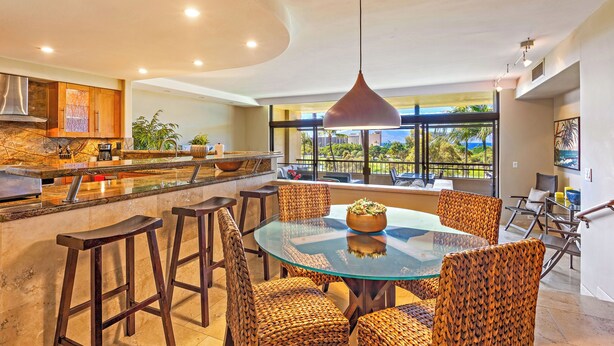 Een moderne keuken met een centraal eiland, barstoelen en een eethoek met rieten stoelen.