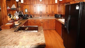 A kitchen with wooden cabinets, a black refrigerator, a microwave, and a marble countertop. - Cloud Nine (St. Augustine)