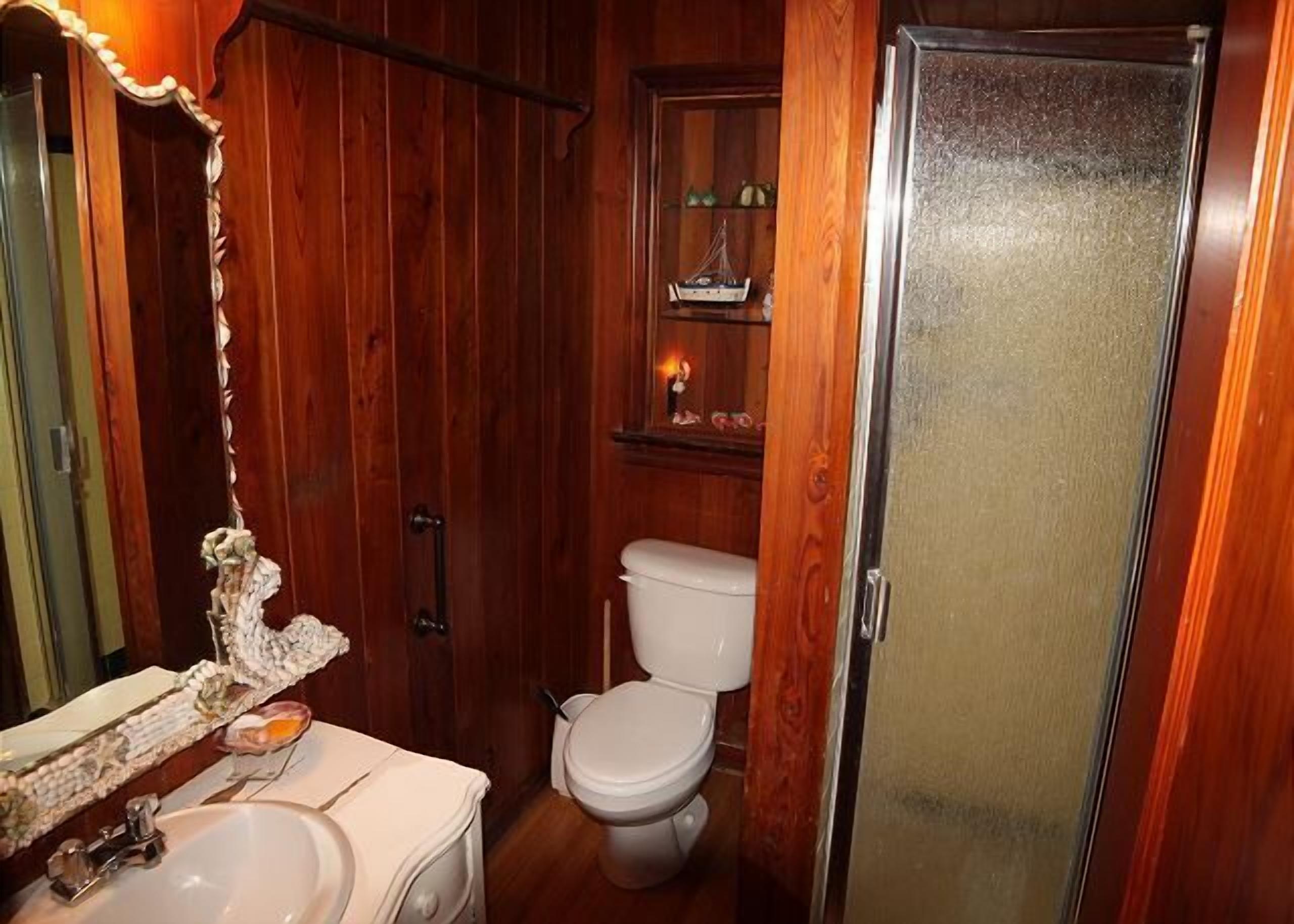Un baño compacto con interior de madera, un lavamanos blanco, un inodoro y un box de ducha de cristal.