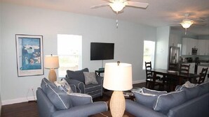 A living room with a ceiling fan, a flat-screen TV, and a dining area with a table and chairs. - Carlapooh - 2018 New Home (St. Augustine)