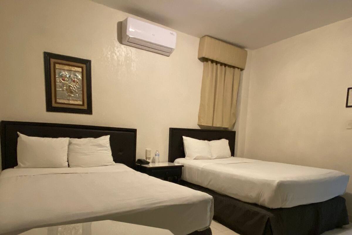 Una habitación de hotel con dos camas individuales, una mesita, un equipo de aire acondicionado y un cuadro en la pared.