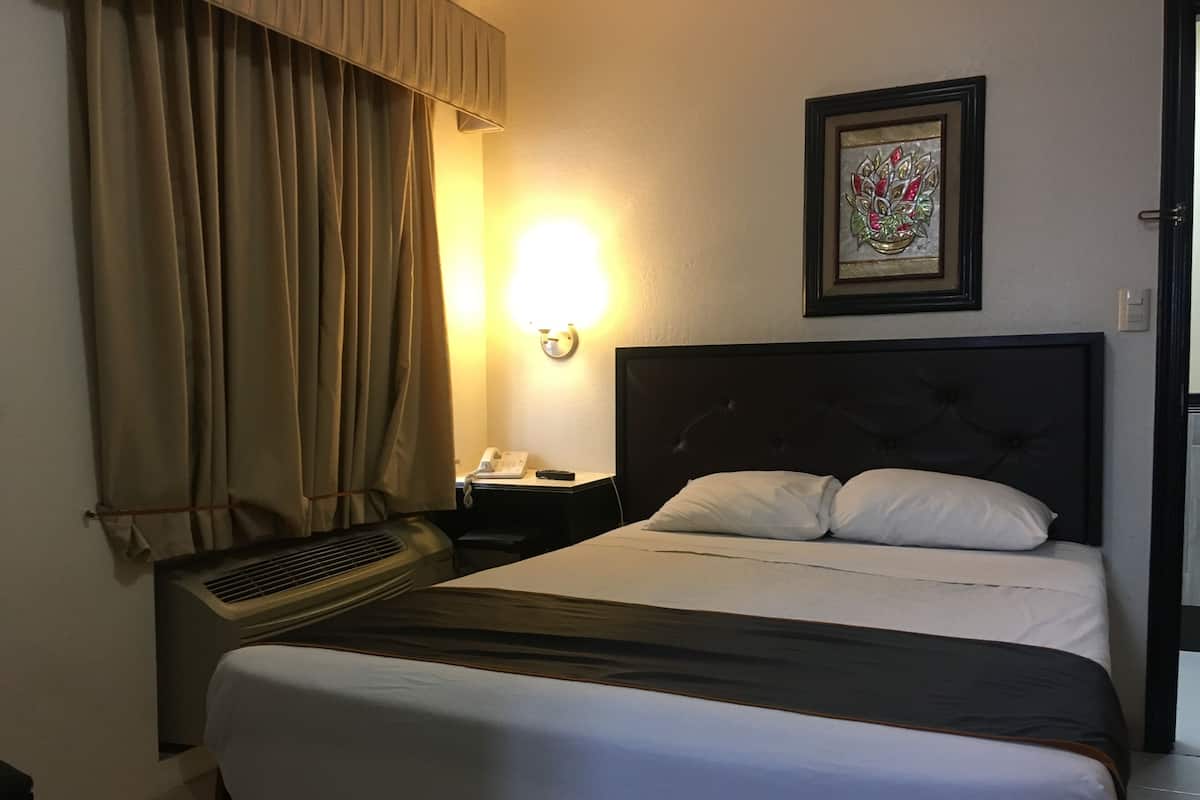 Habitación de hotel con cama, mesita de noche con teléfono, luz de pared y ventana con cortinas.