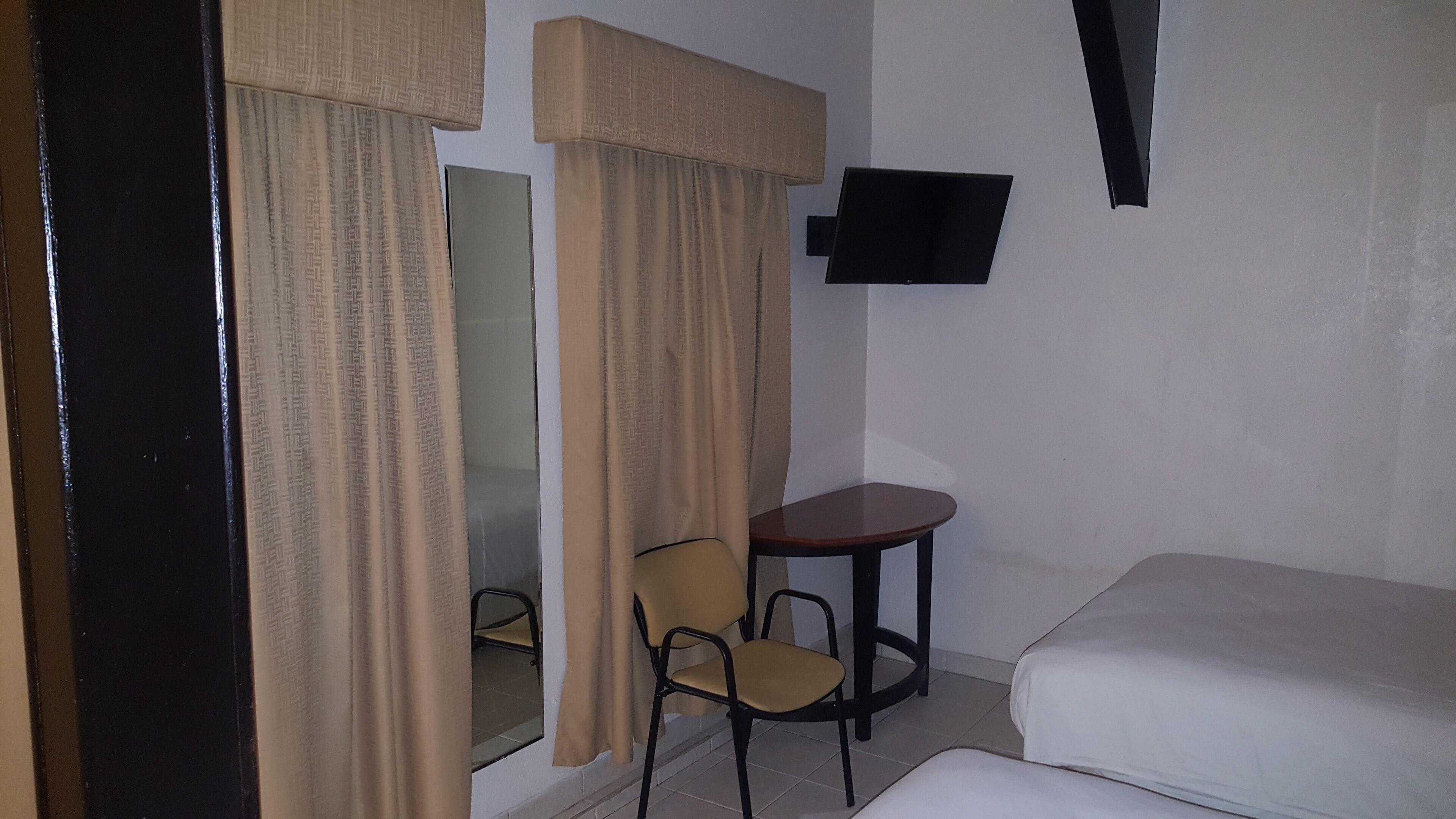 Une chambre d’hôtel avec un lit, une petite table, une chaise et un téléviseur fixé au mur.