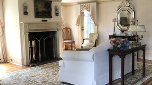 A spacious living room with a fireplace, a sofa, a chair, and a table with decorative items. - Aiken Manor B&B (Franklin)