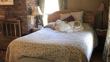 A bedroom with a large bed, a bench, a fireplace, and a window with curtains.