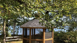 A wooden gazebo with a sloped roof, surrounded by grass and trees, overlooking a body of water. - Aiken Manor B&B (Franklin)