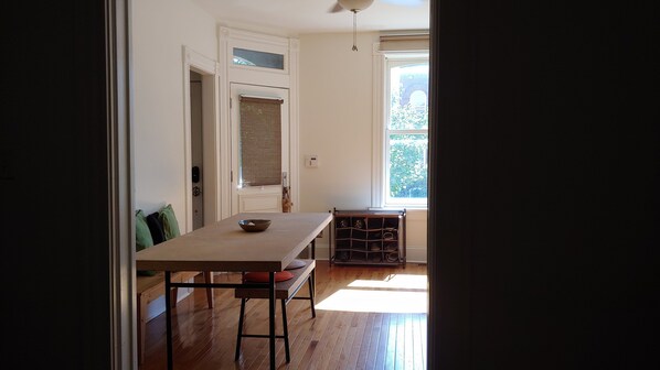A kitchen with a wooden table, a window with a view of greenery, and a door leading to another room.