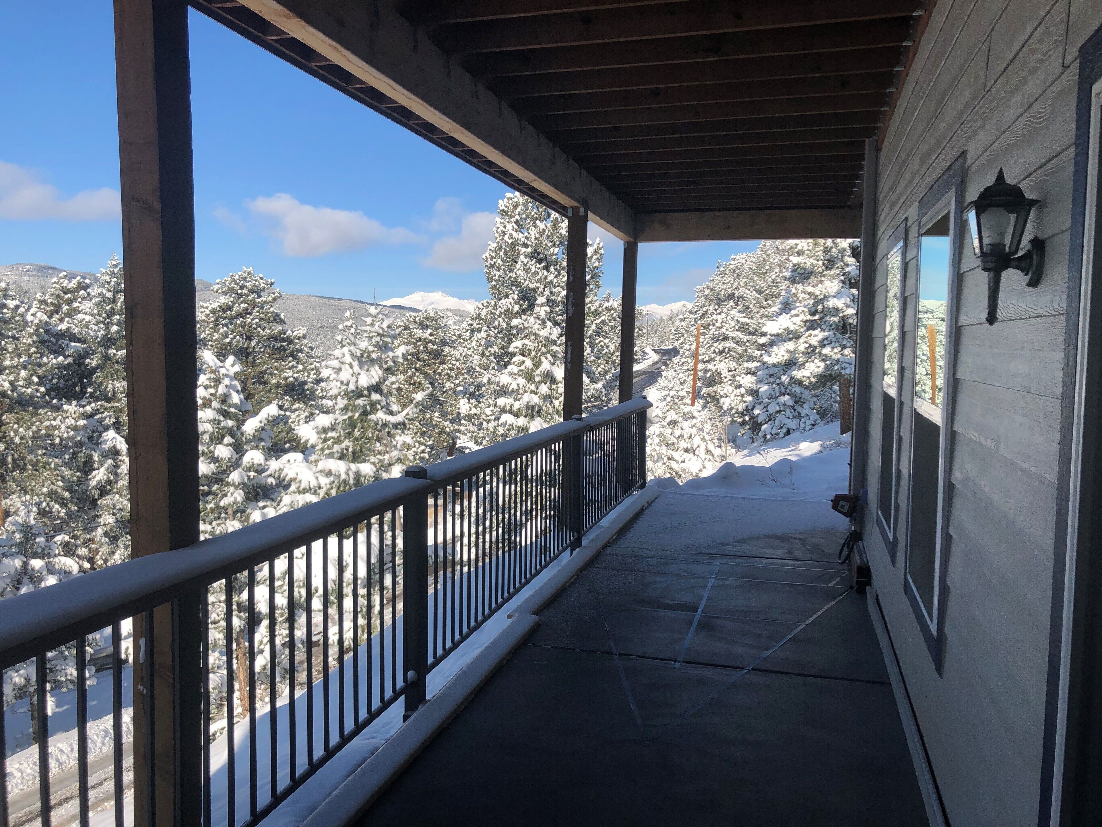 Eine überdachte Veranda mit Metallgeländer, die auf eine verschneite Landschaft mit Bäumen und fernen Bergen blickt.