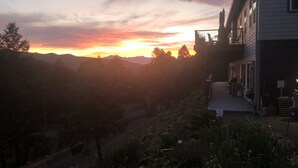 Une maison dotée d’un balcon donnant sur une vallée, avec un coucher de soleil en arrière-plan.