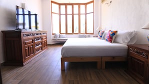Quarto com uma cama grande, cômoda de madeira e televisão sobre um móvel.
