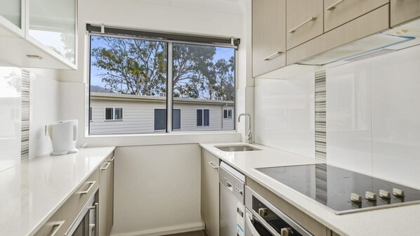 A compact kitchen with a window, white cabinetry, and a dishwasher.