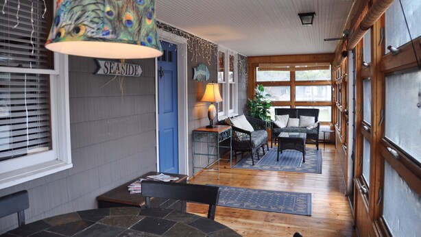 A cozy interior with a dining area, a blue door labeled "SEASIDE," wicker furniture, and a peacock-themed lamp. - Ocean Block Rehoboth Beach House Sleeps 10 (Rehoboth Beach)