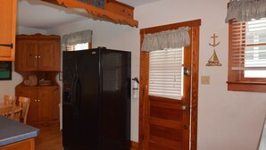 A kitchen with wooden cabinets, a black refrigerator, a wooden door with a window, and a wall-mounted sign above the door. - Ocean Block Rehoboth Beach House Sleeps 10 (Rehoboth Beach)