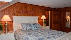 A bedroom with a wooden wall, a bed with a blue floral bedspread, two bedside lamps, and a sign above the bed. - Ocean Block Rehoboth Beach House Sleeps 10 (Rehoboth Beach)
