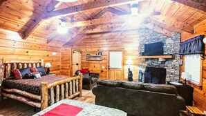 A log cabin interior with a wooden bed, a stone fireplace, and a cozy seating area. - Newly updated cabin, 10 min to pkwy in Pigeon Forge. Screen porch, hot tub,WiFi. (Sevierville)