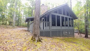 A cabin with a stone chimney, large windows, and a wooden deck surrounded by a forest. - Newly updated cabin, 10 min to pkwy in Pigeon Forge. Screen porch, hot tub,WiFi. (Sevierville)