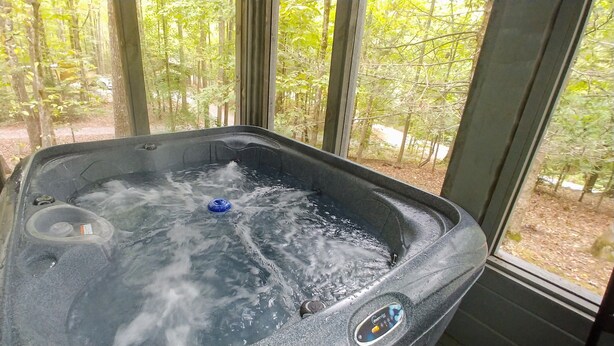 A hot tub with a view of a forest through large windows. - Newly updated cabin, 10 min to pkwy in Pigeon Forge. Screen porch, hot tub,WiFi. (Sevierville)
