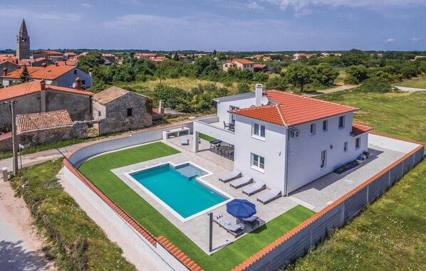 A modern two-story house with a swimming pool, surrounded by a well-maintained lawn and a stone wall.