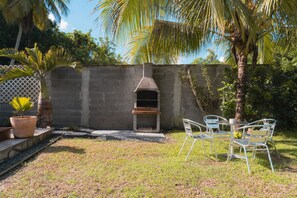 Un jardin avec un mur en briques, un four en béton et une petite table entourée de chaises.