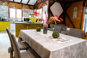 Un coin repas avec une table dressée pour quatre personnes, une cuisine en arrière-plan et un salon avec un canapé et des fauteuils.