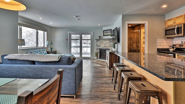A modern kitchen with a stone backsplash, a built-in microwave, and a large island with stools.